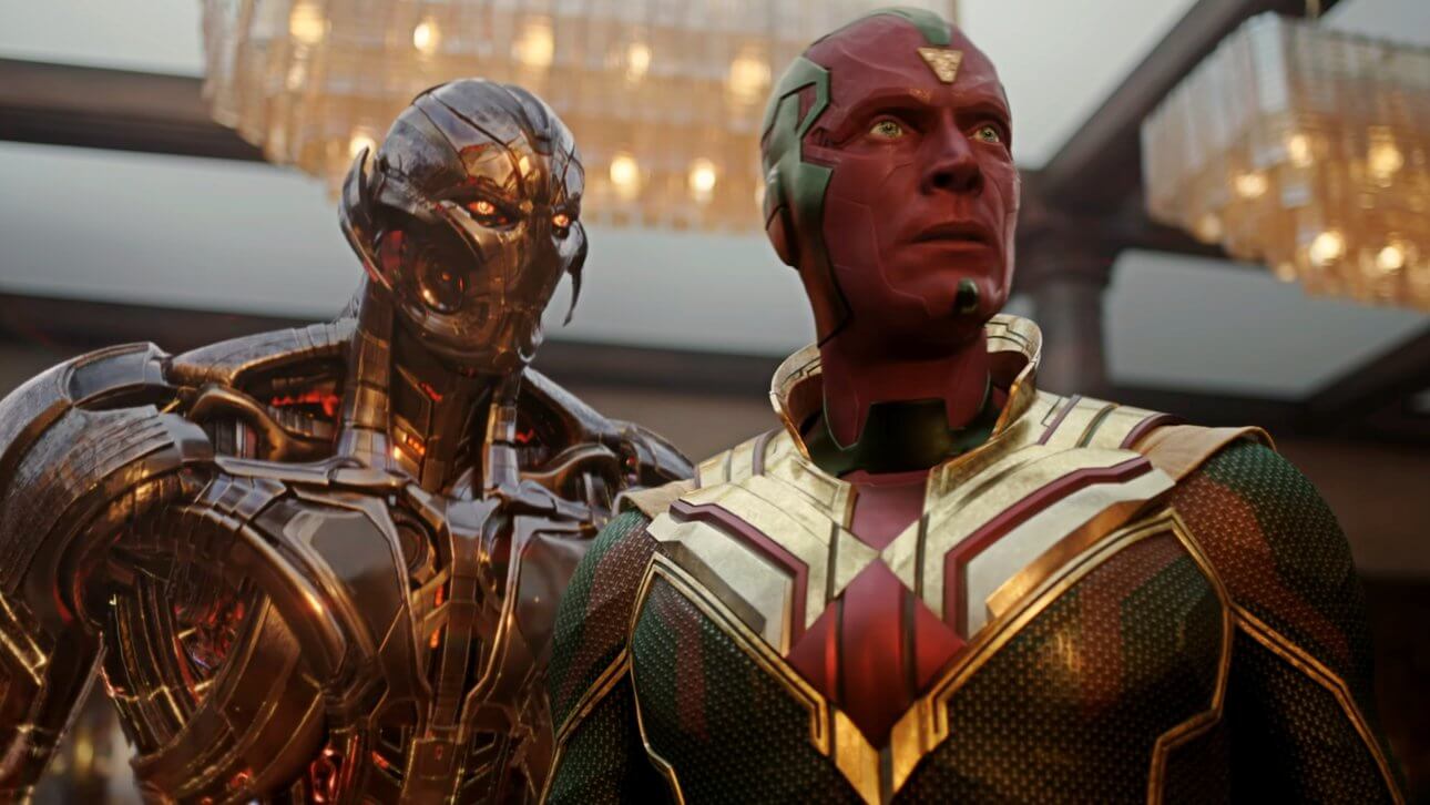 Vision steht mit seinen ikonischen roten, grünen und goldenen Farben in einem Haus. Hinter ihm ist die böse KI Ultron zu sehen, die ihn bedrohlich anstarrt.